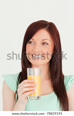 Glad red-haired woman enjoying a glass of orange juice in the kitchen in her apartment
