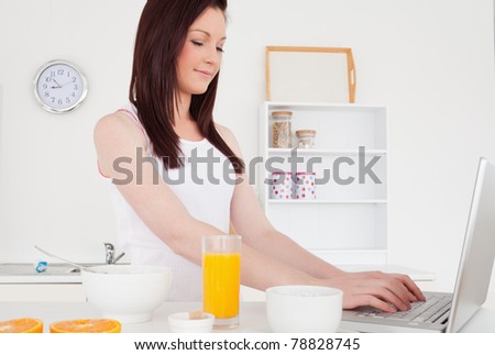 Good looking red-haired female relaxing with her laptop in the kitchen in her apartment
