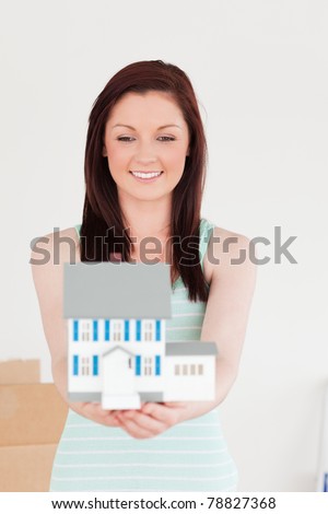 Good looking red-haired woman holding a miniature house while standing on the floor at home