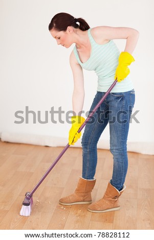 Beautiful red-haired woman sweeping the floor at home