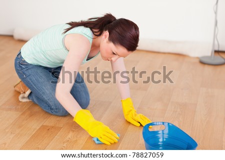 Gorgeous red-haired woman cleaning the floor while kneeling at home