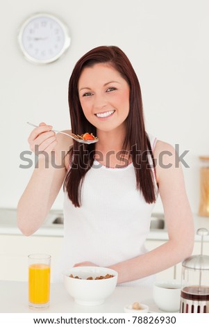Good looking red-haired woman having her breakfast in the kitchen in her apartment