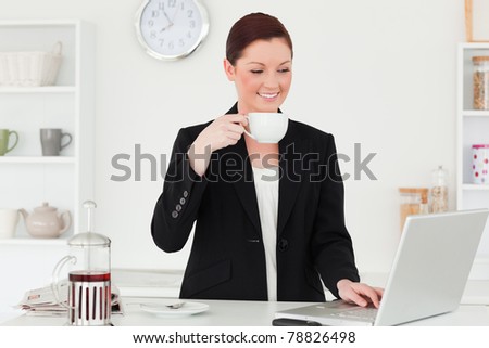 Good looking red-haired woman in suit relaxing with her laptop in the kitchen in her apartment
