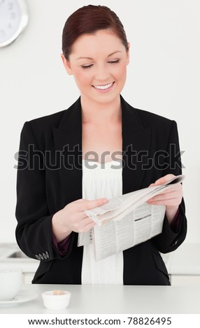 Beautiful red-haired woman in suit reading the newspaper in the kitchen in her apartment