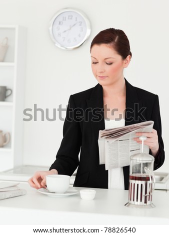 Gorgeous red-haired woman in suit reading the newspaper in the kitchen in her apartment
