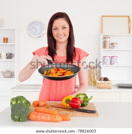 Gorgeous red-haired woman cooking vegetables in the kitchen in her apartment