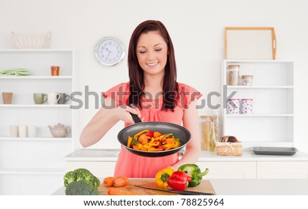 Pretty red-haired woman cooking vegetables in the kitchen in her apartment
