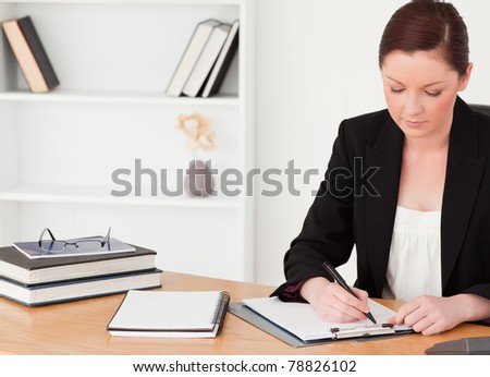 Attractive red-haired woman in suit writing on a notepad while sitting in an office