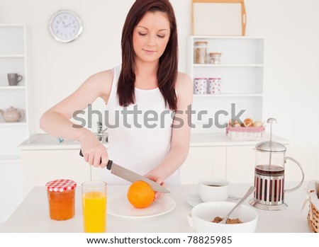 Young good looking red-haired woman cutting an orange in the kitchen in her apartment