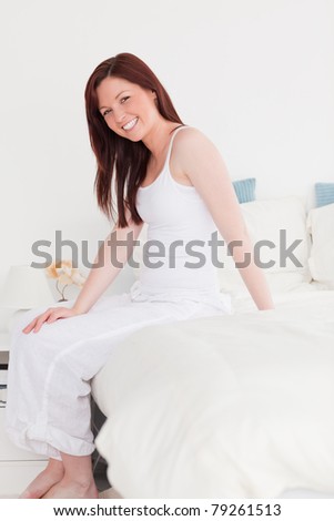 Good looking red-haired female posing while sitting on her bed