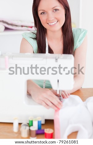 Pretty red-haired woman using a sewing machine in her living room