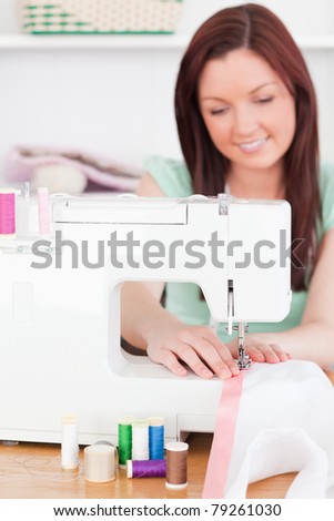 Gorgeous red-haired woman using a sewing machine in her living room