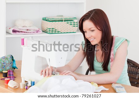 Pretty red-haired female using a sewing machine in her living room