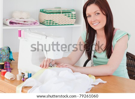 Attractive red-haired female using a sewing machine in her living room