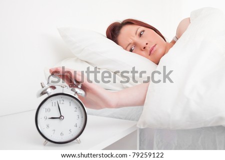 Beautiful red-haired female waking up thanks to an alarm clock in the bedroom