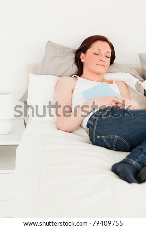 Pretty female having a rest while holding a book on her bed