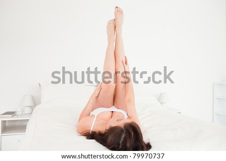 Good looking brunette female stretching her legs while lying on a bed
