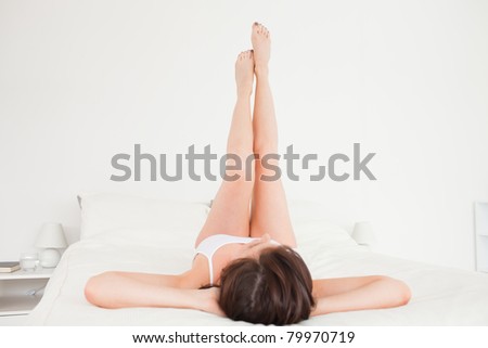 Attractive brunette female stretching her legs while lying on a bed