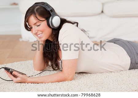 Gorgeous brunette female listening to music with her music player while lying on a carpet in the living room