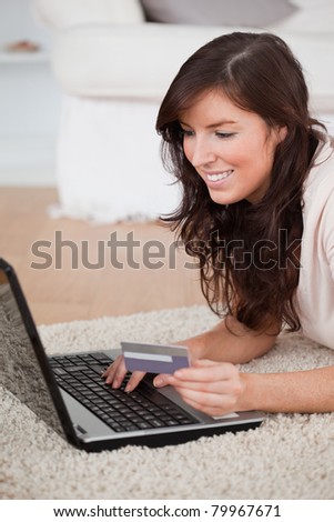 Young attractive woman making a payment with a credit card on the internet while lying on a carpet in the living room
