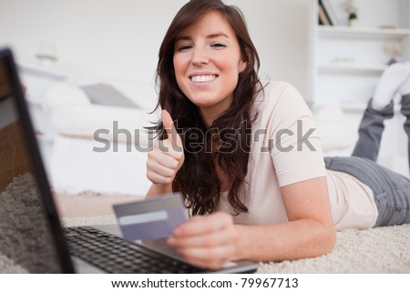 Young cute woman making a payment with a credit card on the internet while lying on a carpet in the living room