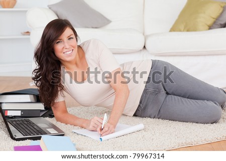 Young cute woman relaxing with her laptop while writing on a notebook in the living room