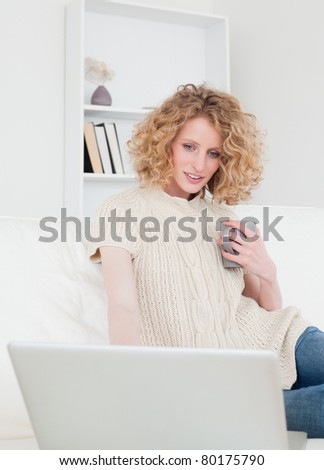 Cute blonde woman relaxing with her laptop while sitting on a sofa in her apartment