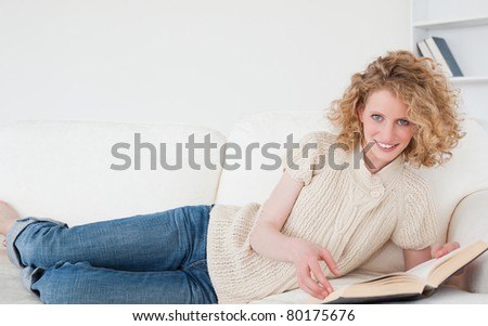 Pretty blonde woman reading a book while lying on a sofa in her apartment