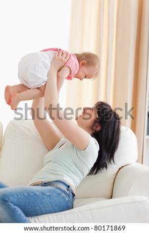 Gorgeous woman holding her baby in her arms while sitting on a sofa in the living room