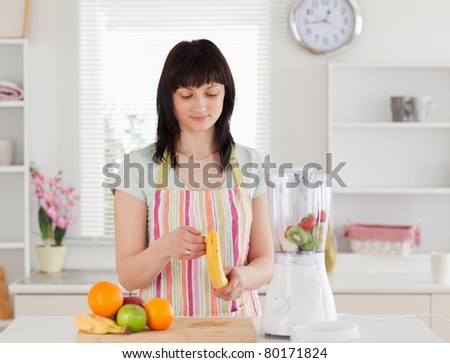 Good looking brunette woman pealing a banana while standing in the kitchen