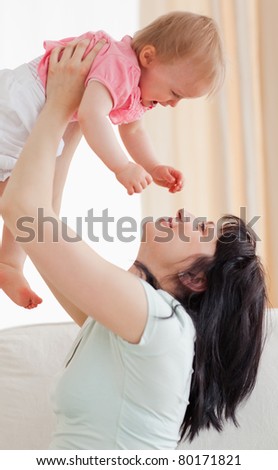 Cute woman holding her baby in her arms while sitting on a sofa in the living room