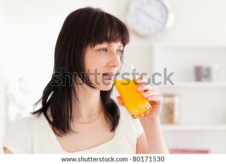 Good looking brunette drinking a glass of orange juice while standing in the kitchen