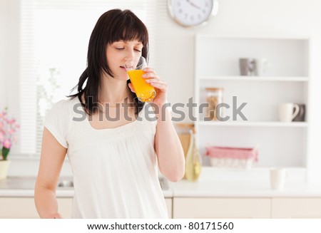 Lovely brunette drinking a glass of orange juice while standing in the kitchen