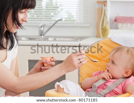 Beautiful brunette woman feeding her baby while sitting in the kitchen