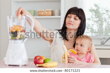 Pretty brunette woman pealing a banana while holding her baby on her knees in the kitchen