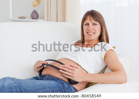 Happy pregnant woman with headphones on her belly looking at the camera
