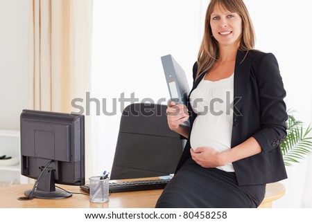Pretty pregnant female holding a file while standing in the office