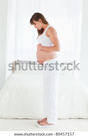 Attractive pregnant female using a scale while standing in her bedroom