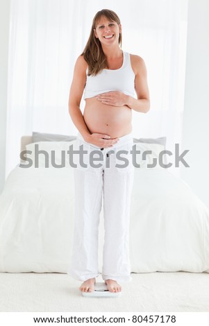 Beautiful pregnant female using a scale while standing in her bedroom