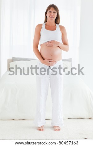 Beautiful pregnant female posing while standing in her bedroom