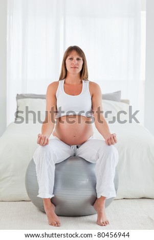 Beautiful pregnant female doing relaxation exercises while sitting on a gym ball in her bedroom
