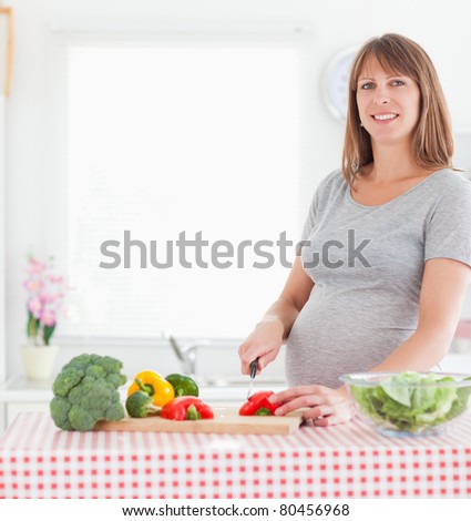 Good looking pregnant woman posing while cooking vegetables in a kitchen
