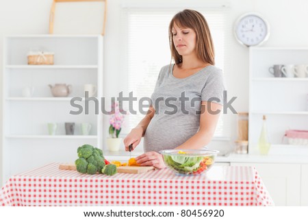 Lovely pregnant woman posing while cooking vegetables in a kitchen