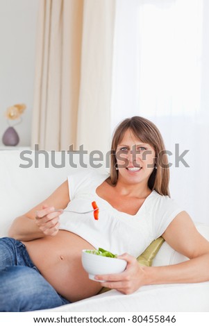 Portrait of a pregnant woman eating a salad in her living room