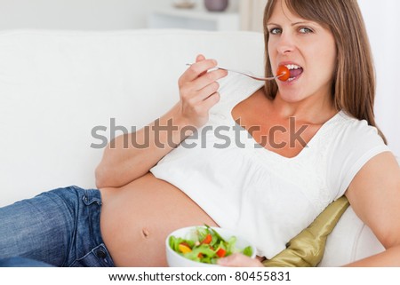 Close up of a happy pregnant woman eating a salad in her living room