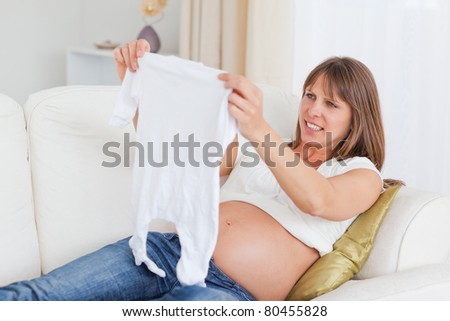 Beautiful pregnant woman holding a baby grow while lying on a sofa in her living room