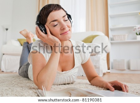 Delighted woman with a magazine enjoying some music while lying on a carpet
