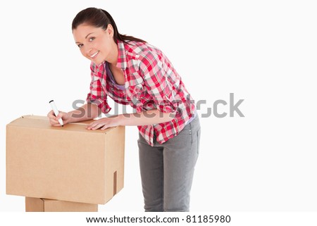 Beautiful woman writing on cardboard boxes with a marker while standing against a white background
