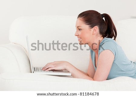 Side view of a beautiful woman relaxing with her laptop while lying on a sofa in the living room