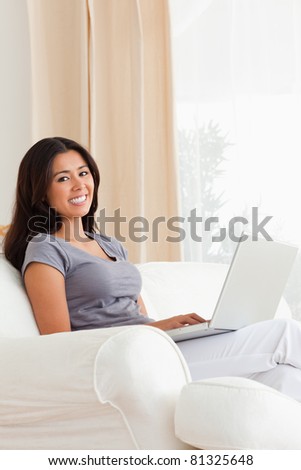 smiling woman sitting on sofa with notebook looking into camera in living room